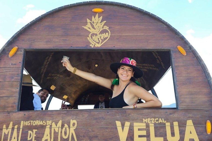 A wooden structure with the text 'MAI DE AMOR' and 'MEZCAL VELUA' on it. 2