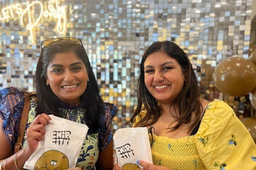 Two people holding bags with 'CHIP CITY' printed on them, standing in front of a disco ball and balloons. 2
