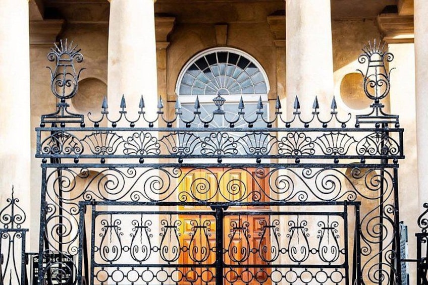 A wrought iron gate with intricate designs, a stone archway, and a circular window above. 3