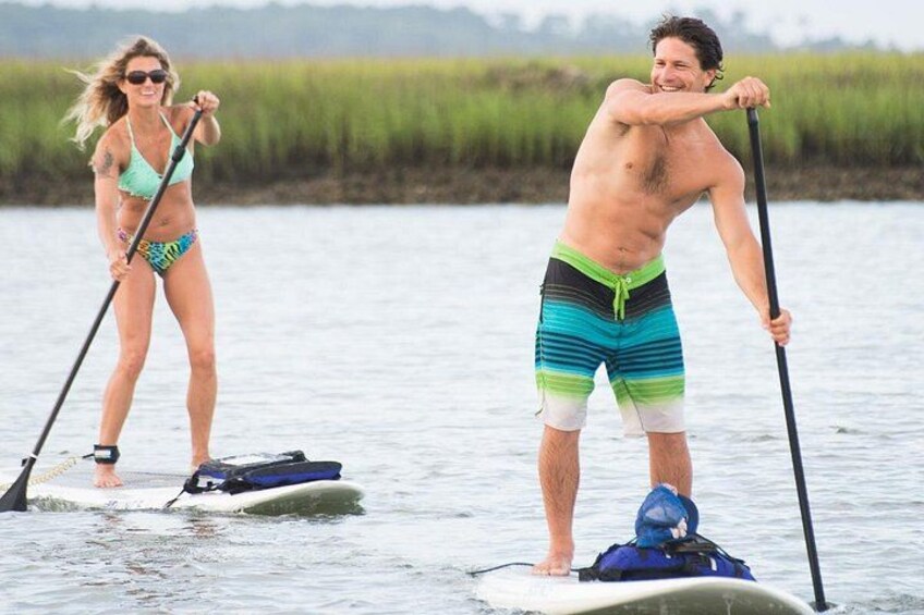Deux personnes pratiquent le stand-up paddle sur une étendue d’eau calme, avec des berges verdoyantes en arrière-plan. 2