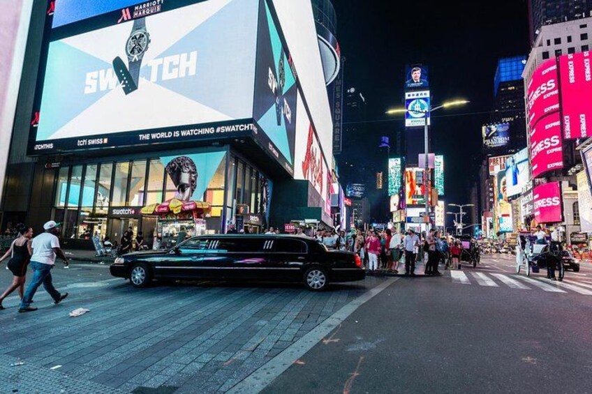 A busy urban street at night with illuminated billboards and a prominent Swatch advertisement. 2