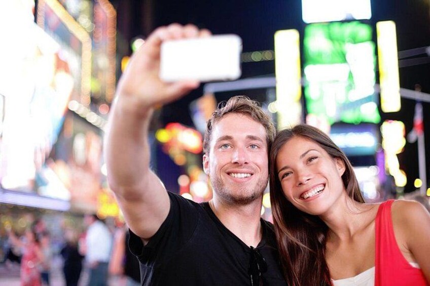 En person som tar en selfie tillsammans med en annan person i en väl upplyst stadsmiljö med neonreklamer. 3
