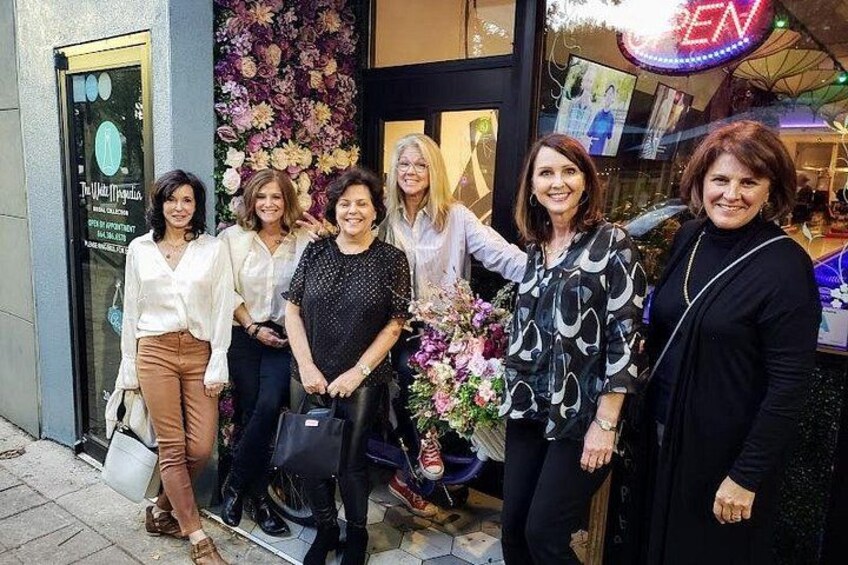 Een groep mensen staat voor een winkel met een bloemendecoratie en een neonreclame. 4