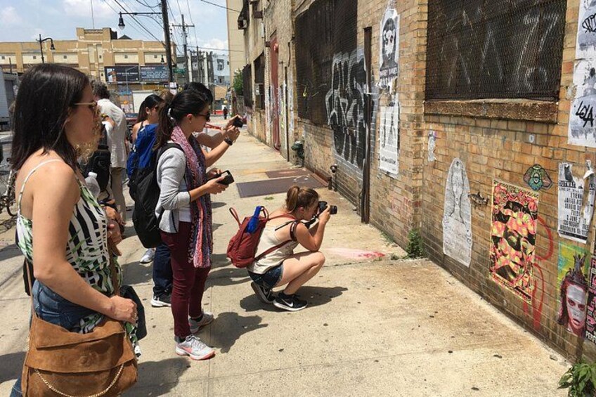A group of people taking photos on a street with graffiti-covered walls. 2
