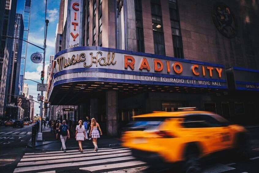 The Music Hall Radio City building with a crosswalk and a yellow taxi in motion. 3