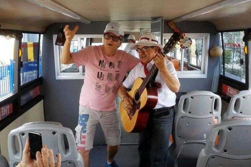 Twee personen in een bus, waarvan er één gitaar speelt en de ander gebaart. 4