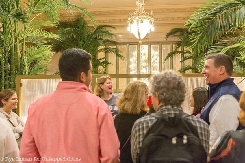 A group of people in a lobby with a chandelier and palm plants. 4