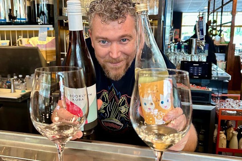 A person holding two bottles of wine and two glasses, one with wine and one with a drink. 3