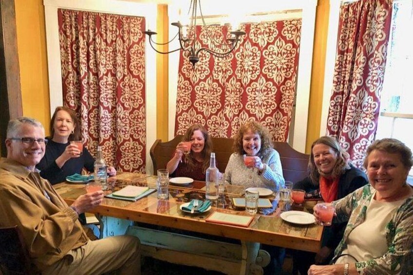 A group of people sitting around a wooden dining table with red patterned curtains in the background. 4