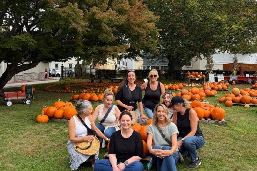 A group of people sitting on grass with pumpkins in the background. 5