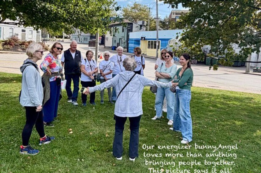A group of people holding hands in a circle on a grassy area with buildings in the background. 4