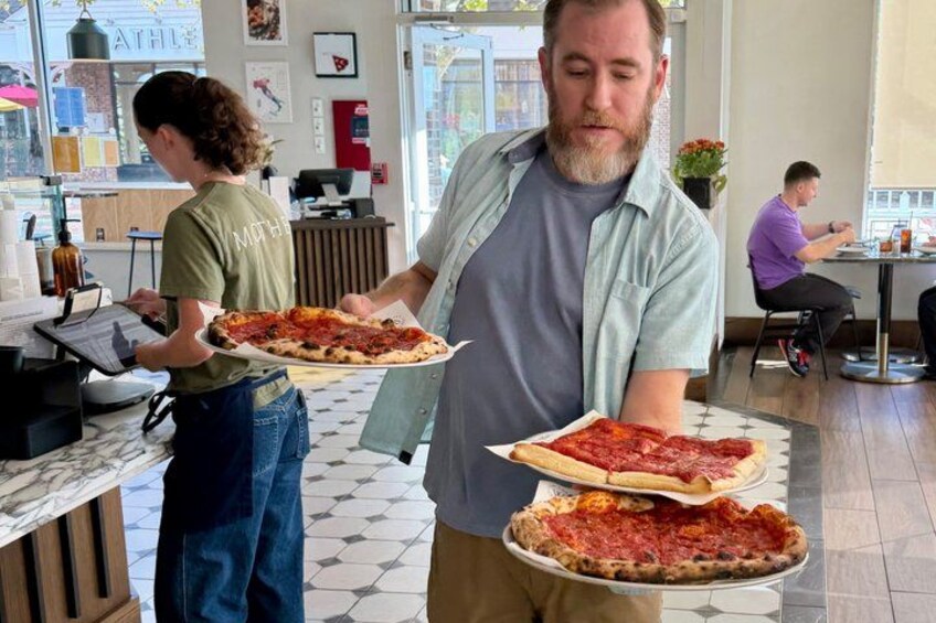 A person holding a pizza in a restaurant with another person in the background. 2