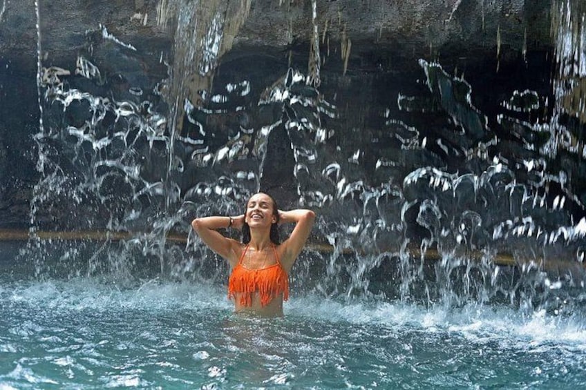 A person in a pool with water splashing around them, with a rocky background. 3