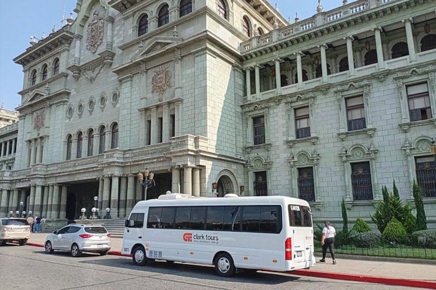 A white tour bus parked in front of a large, ornate building with columns and statues. 2