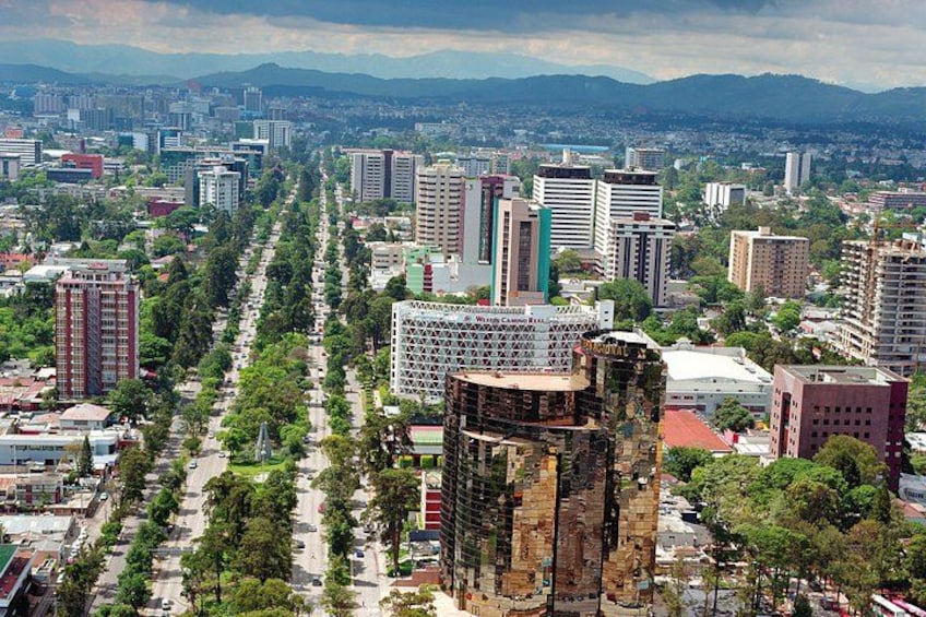 A cityscape with a prominent tower, a tree-lined avenue, and a distant mountain range. 3