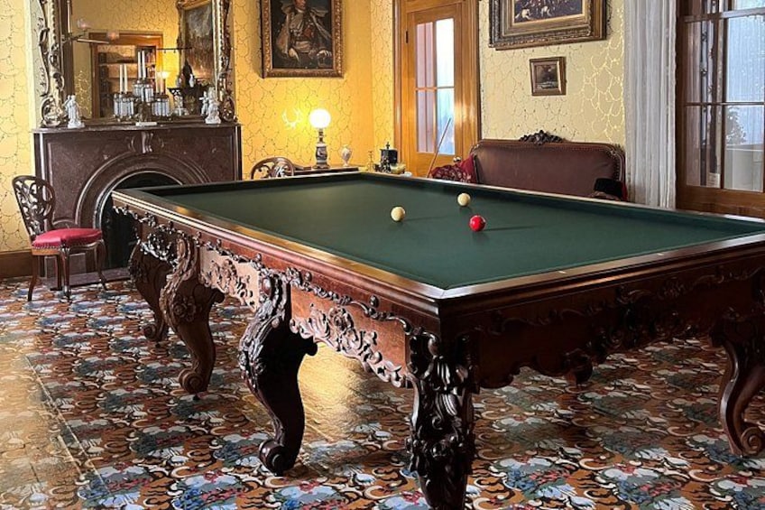 A pool table with balls, a fireplace, and ornate chairs in a room with patterned flooring. 3