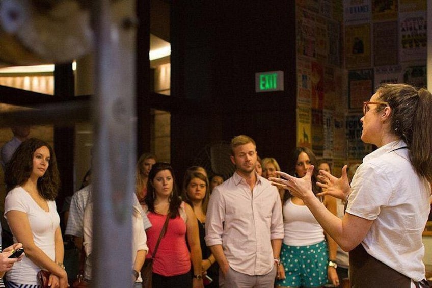A person speaking to a group of people in a public indoor space with an exit sign above. 3