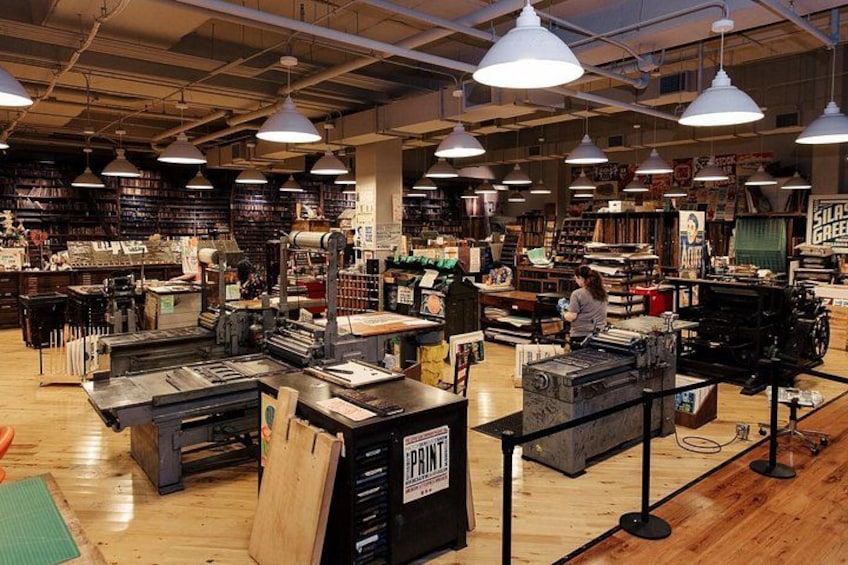 A bookstore with shelves of books, tables with printing equipment, and a person working at a table. 5