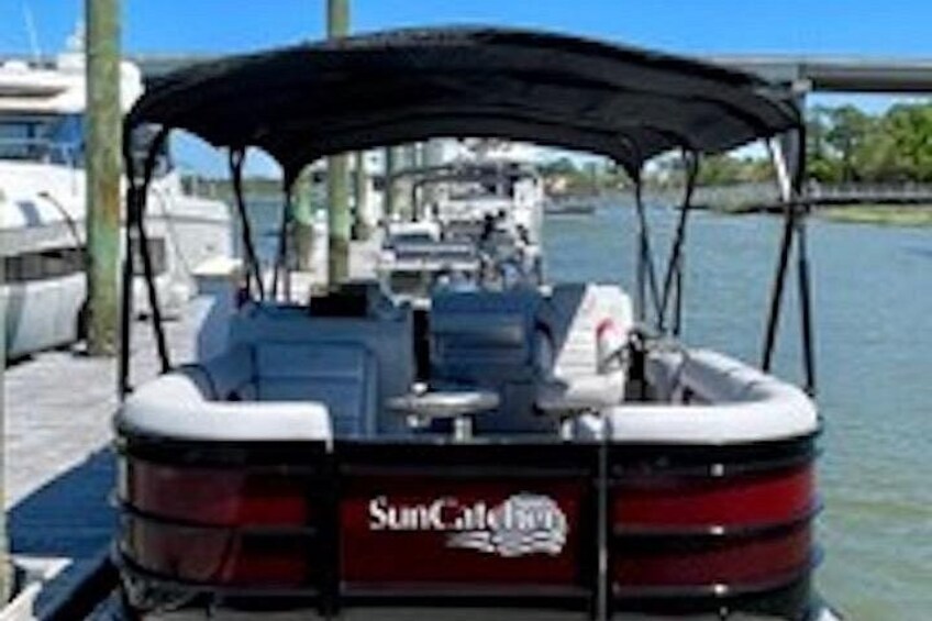 A boat docked at a marina with a canopy, water, and other boats in the background. 2