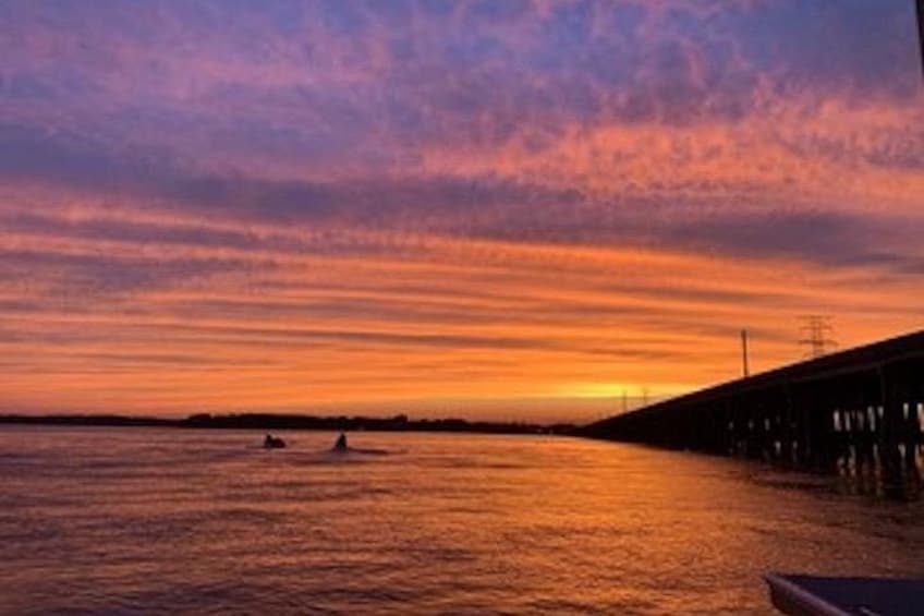 A sunset over a body of water with a bridge in the background. 1