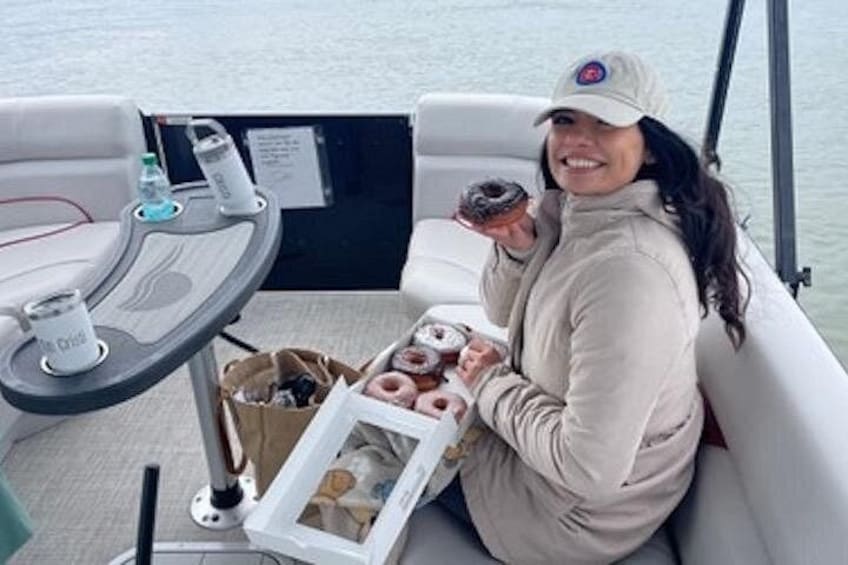 Une personne à bord d’un bateau, tenant un beignet, avec un plateau de beignets et une bouteille d’eau visibles. 2