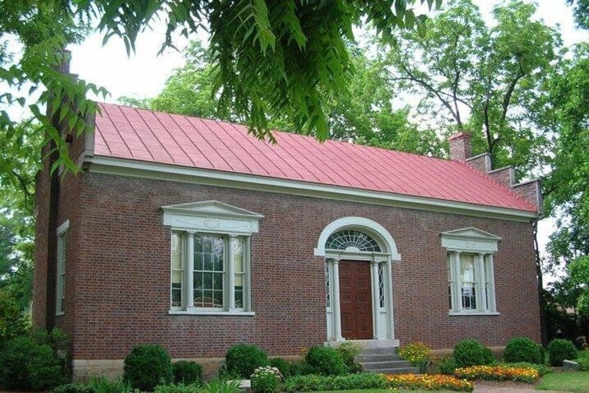 Een bakstenen huis met een rood dak, witte sierlijsten en een centraal rondboogvenster. 2