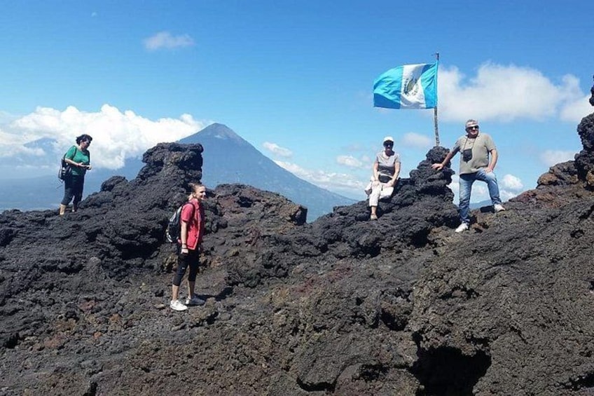 People on a volcanic landscape with a flag, a volcano in the background, and a clear sky. 5