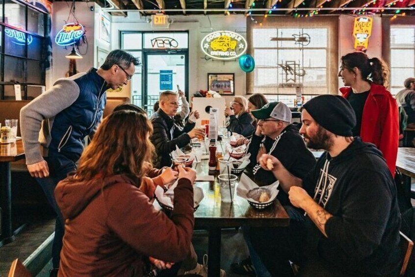 A group of people dining at a restaurant with a neon sign in the background. 1