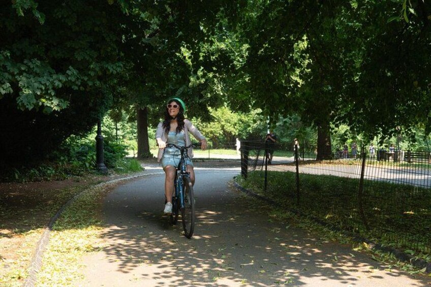 Une personne fait du vélo sur un chemin aménagé dans un parc, où l’on peut voir des arbres et une clôture. 5