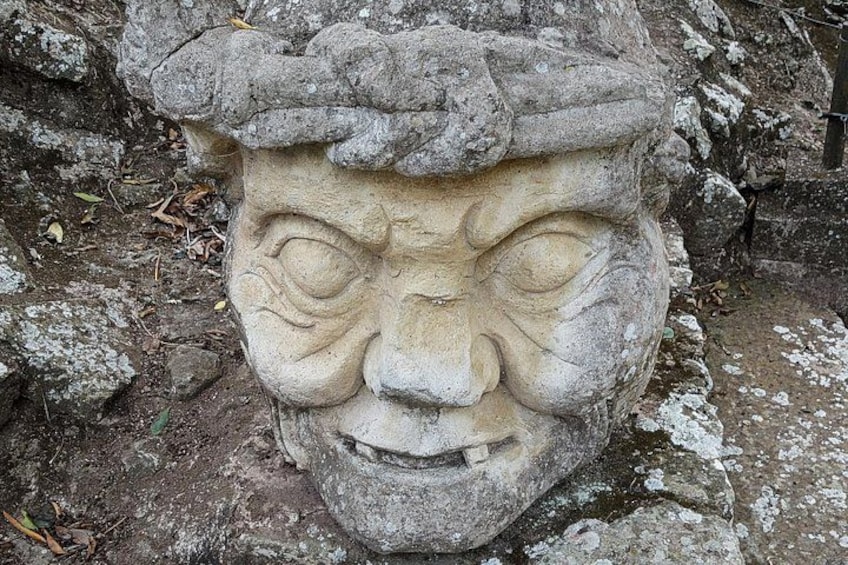 A stone face sculpture with a rough texture, surrounded by a rocky and uneven ground. 5