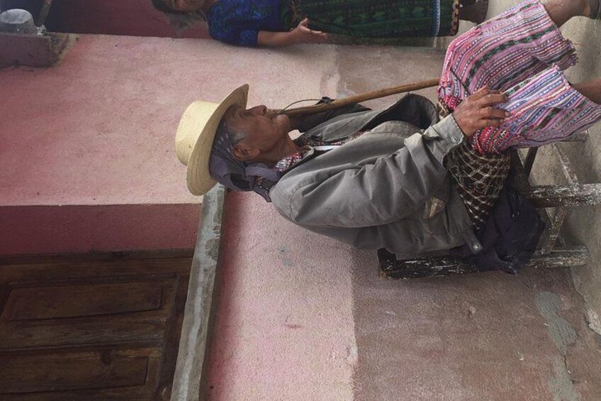 A person sitting on a bench, wearing a hat and a jacket, holding a patterned bag. 2