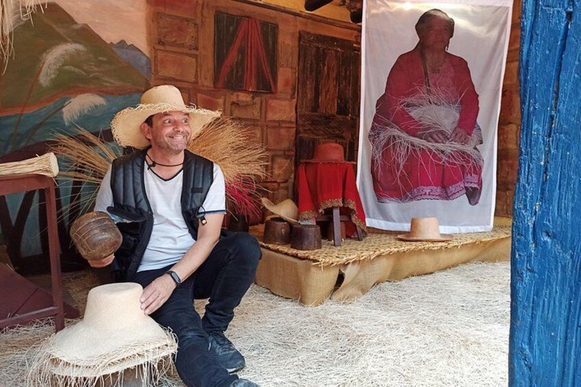A person sitting on straw, holding a ball, with a poster and straw hats in the background. 1