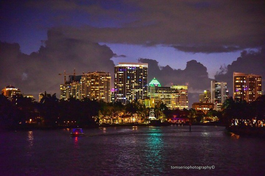 A city skyline at night with illuminated buildings and a body of water reflecting the lights. 3