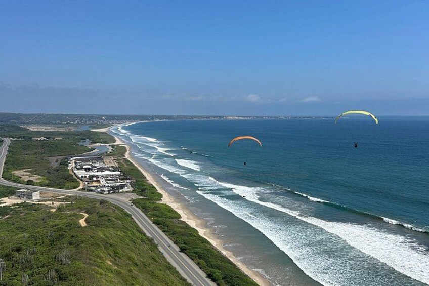 Una carretera costera con una playa, un complejo de edificios y parapentistas a lo lejos. 5