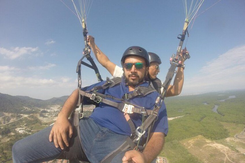 Een persoon paragliding, vastgehouden aan de lijnen, met een harnas en parachute, met een bergachtig landschap op de achtergrond. 1