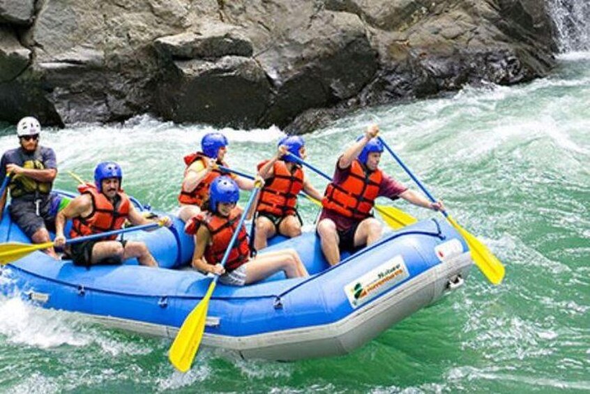 A group of people in a blue inflatable raft on a river, paddling with yellow paddles. 3