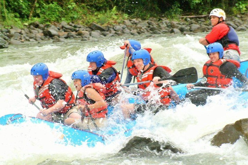 A group of people in a blue raft navigating a river with white water rapids. 5