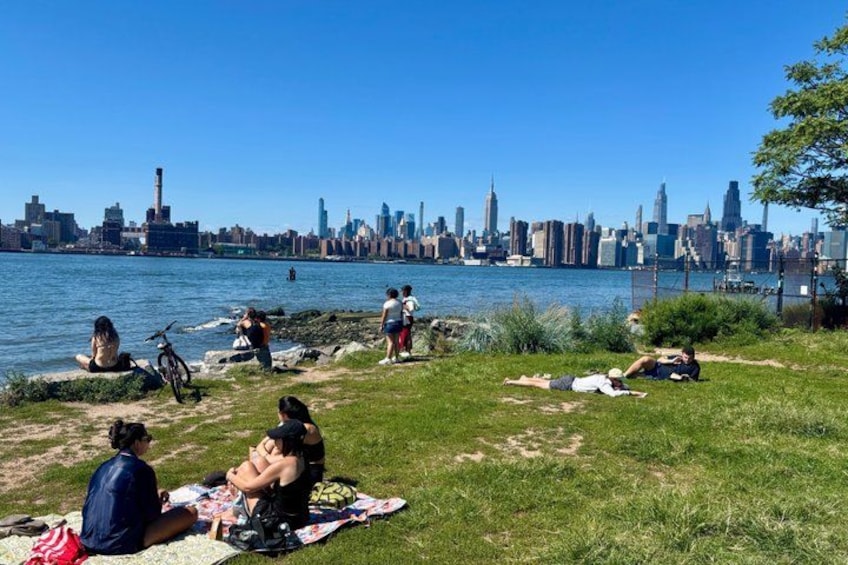 A riverside park with people relaxing on blankets, a bicycle, and a city skyline in the background. 5