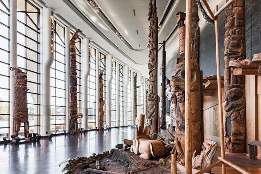 A museum interior with large windows, wooden sculptures, and a polished floor. 1