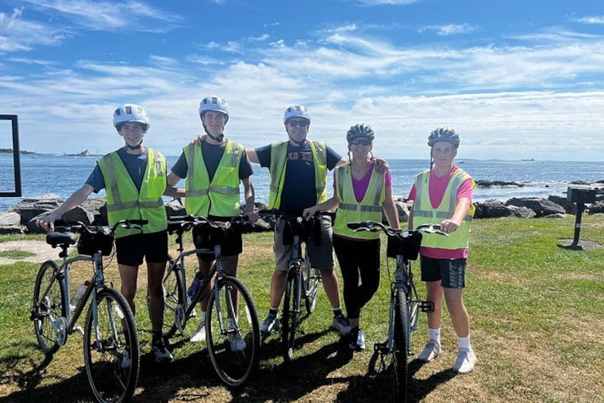 Quatre personnes à vélo, portant des gilets de sécurité, se tiennent sur l’herbe, près d’une étendue d’eau. 1