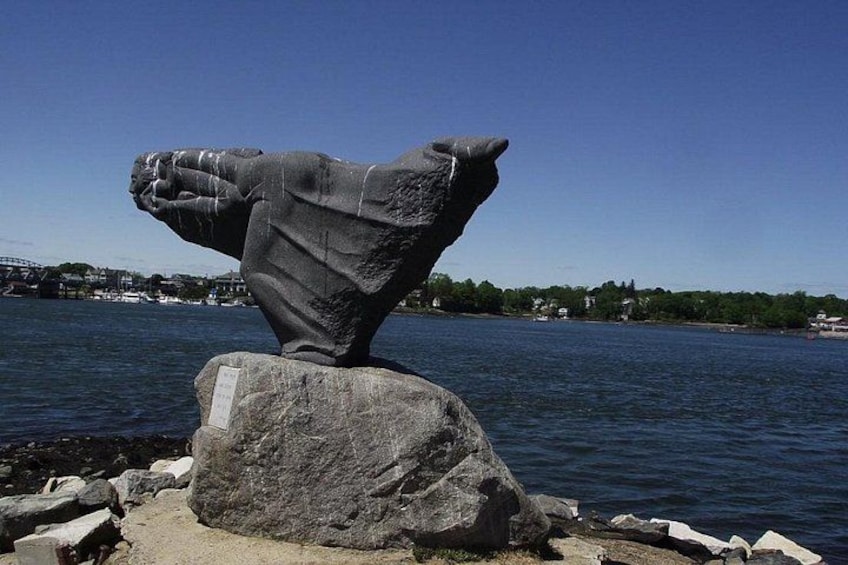 A stone sculpture of a hand on a rock by a body of water. 5