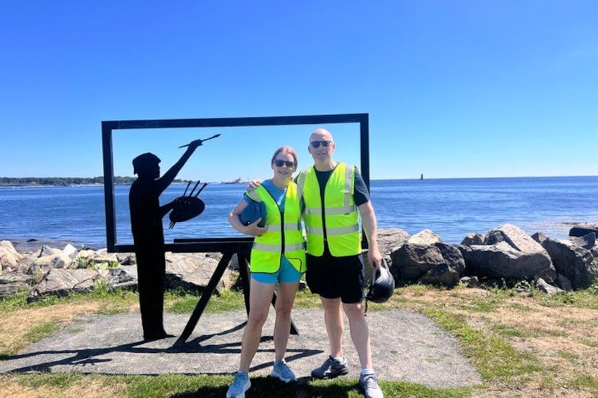 Deux personnes se tiennent devant une grande œuvre d’art représentant une silhouette, avec une étendue d’eau et des rochers en arrière-plan. 5
