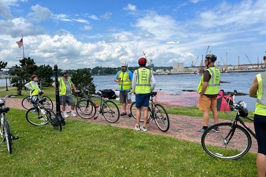 A group of cyclists at a waterfront, wearing safety vests, with bicycles and a flag in the background. 3