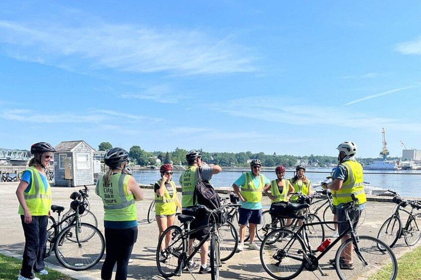 A group of people wearing safety vests and helmets, standing by bicycles near a waterfront. 5