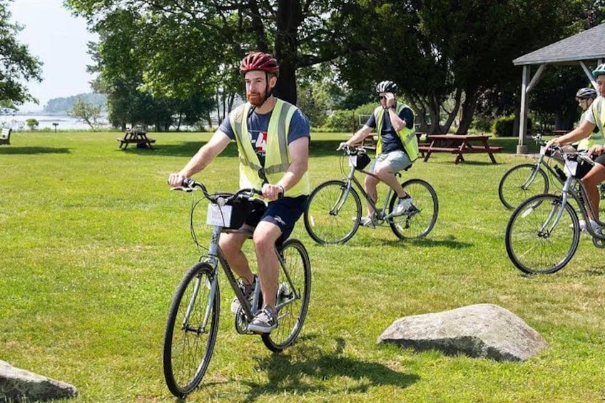 Three cyclists on a grassy field with a picnic table and a gazebo in the background. 2