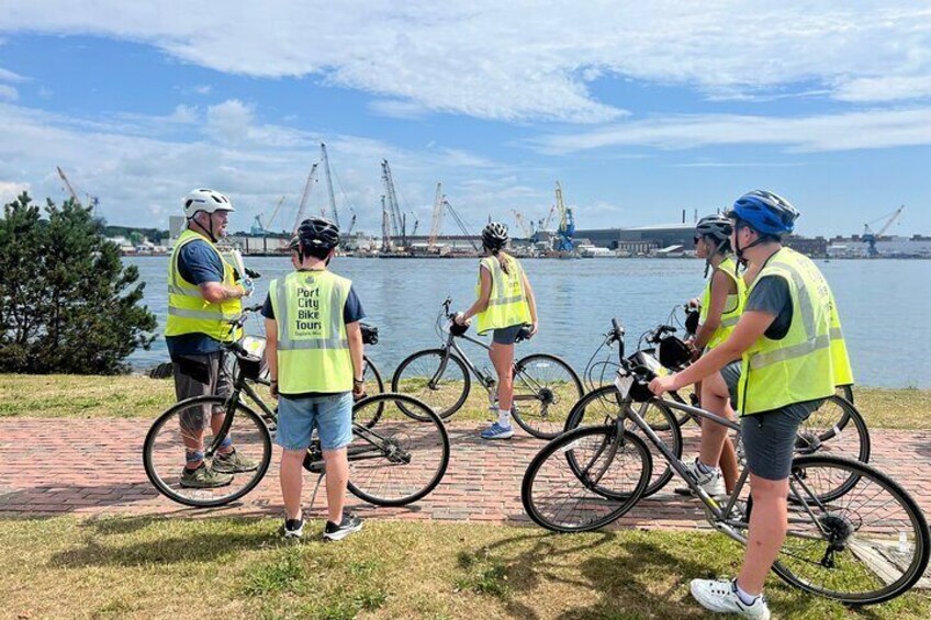 Un grupo de personas en bicicletas cerca de la costa, con grúas al fondo. 2