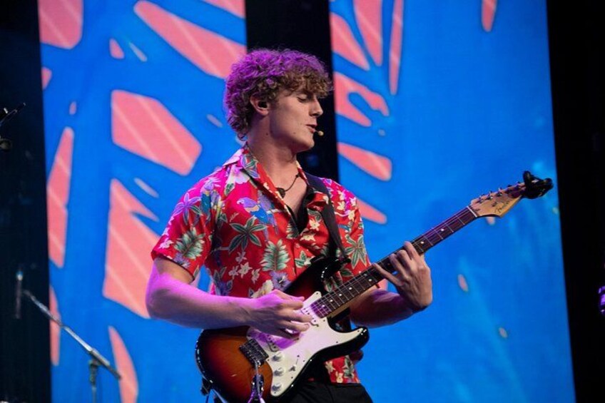 En person som spelar elgitarr på en scen med en färgglad bakgrund. 4