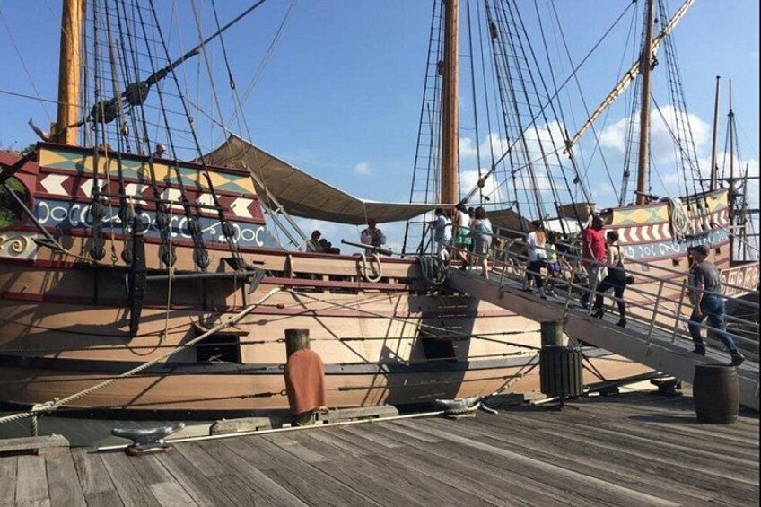 A wooden deck with a ship's rigging, a lifeboat, and people walking. 2