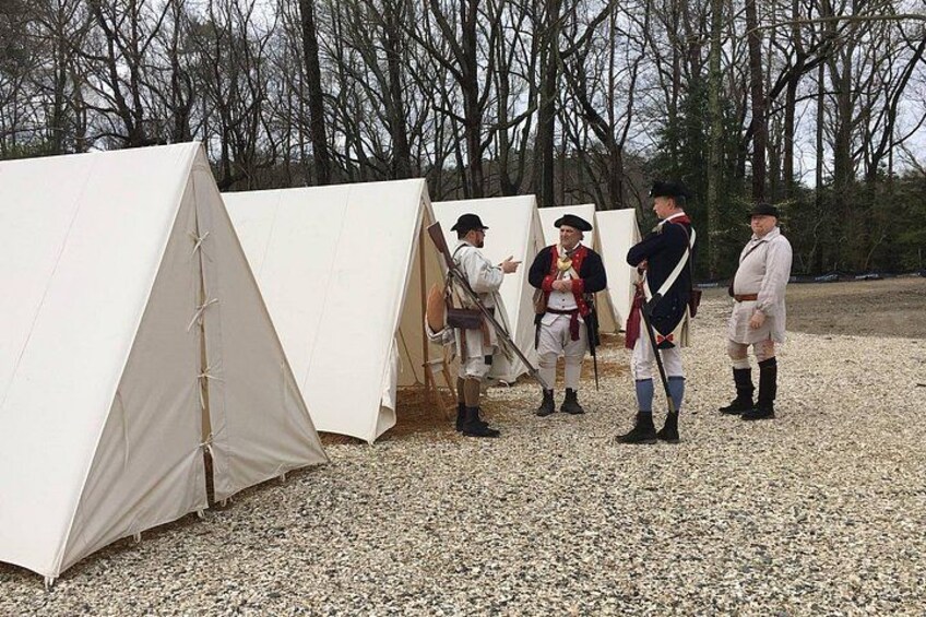 A historical reenactment with individuals in period costumes standing near tents in an outdoor setting. 3