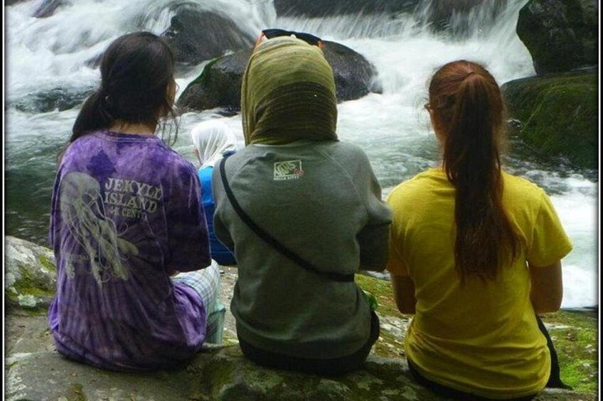 Tres personas sentadas sobre rocas junto a una cascada. 1